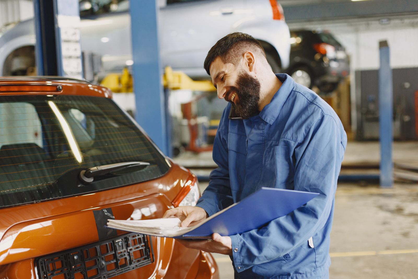 Auto service technician taking a phone call beside a car in the shop